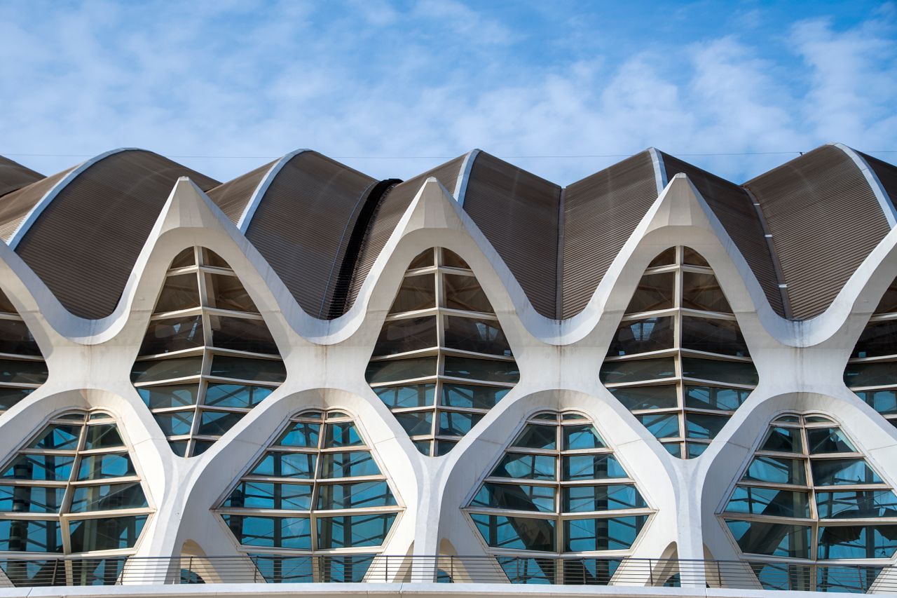 services-04 Close-up of a modern architectural facade featuring wave-like geometric patterns against a blue sky.